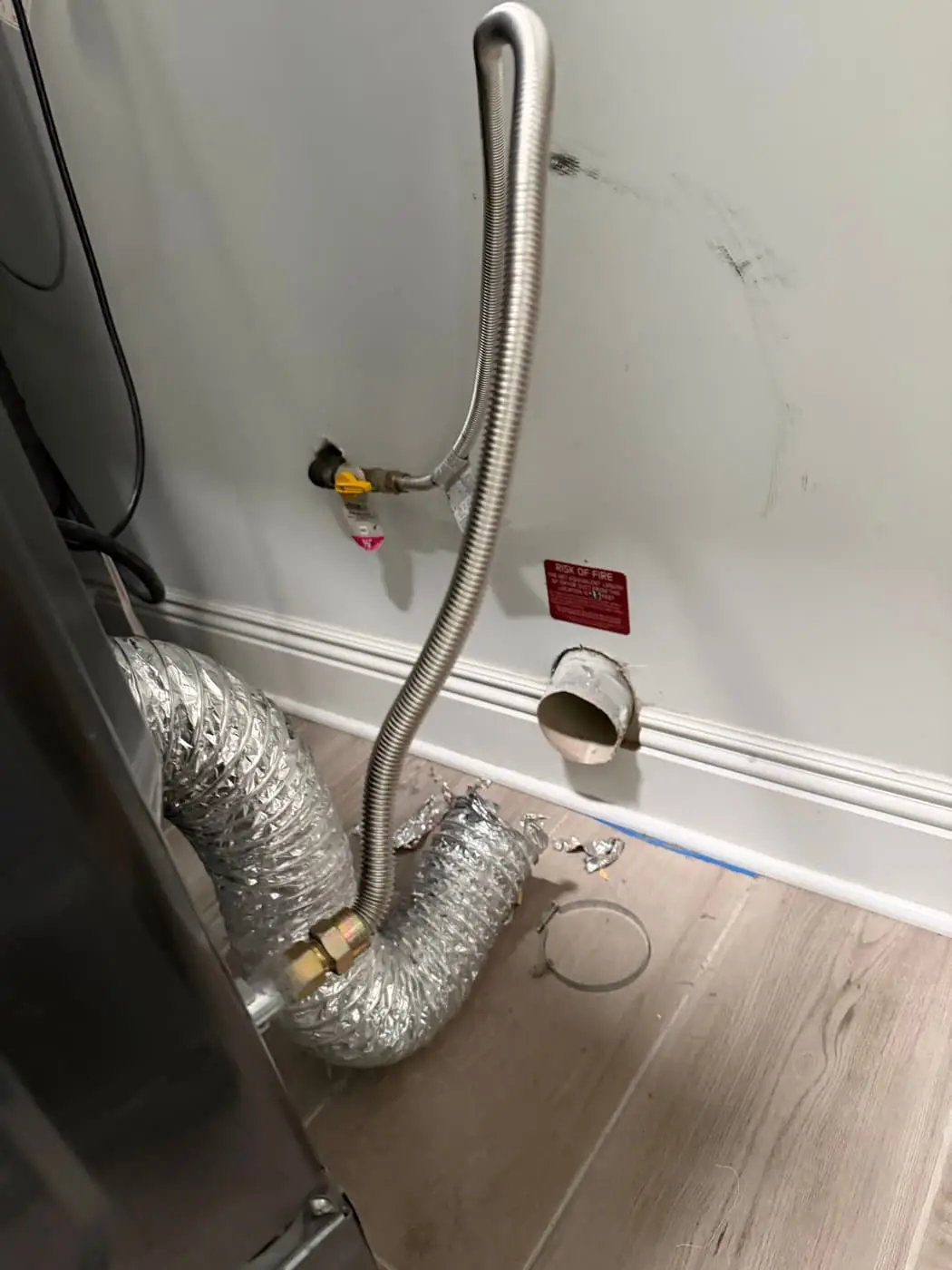 A foil dryer duct and a gas line behind a dryer, connected to the wall.
