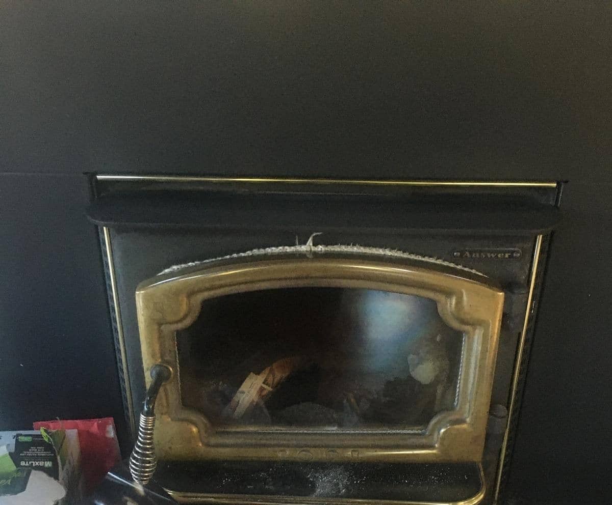 A fireplace insert with a gold-trimmed glass door set into a black surround.