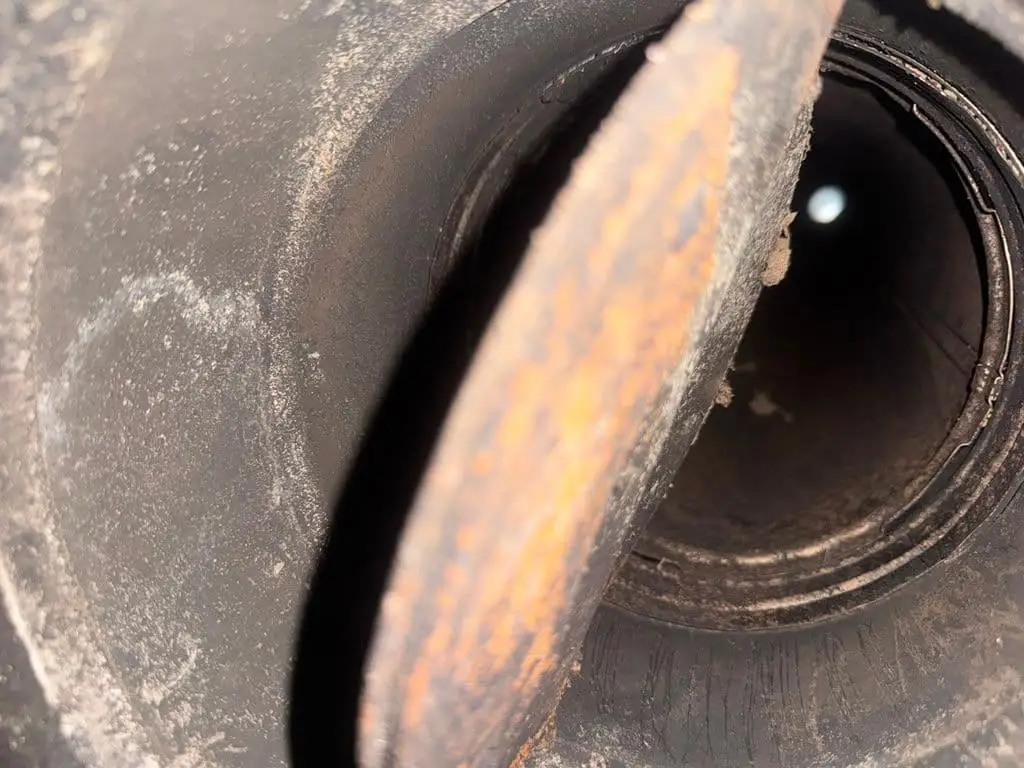 Looking into a round metal flue past a rusted damper plate.